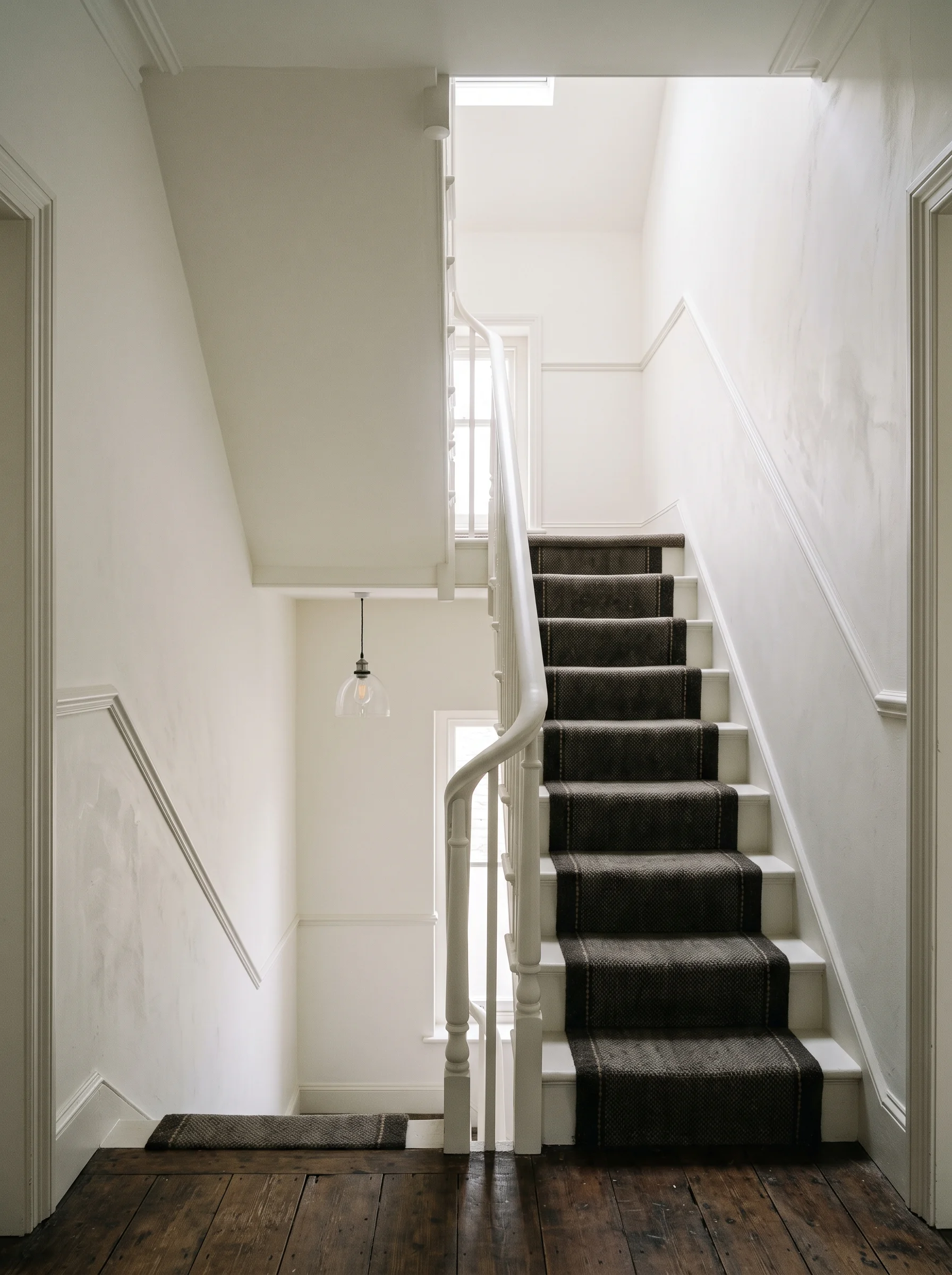 Terraced hallway and stairwell freshly painted in slaked-lime white, light falling from a landing window