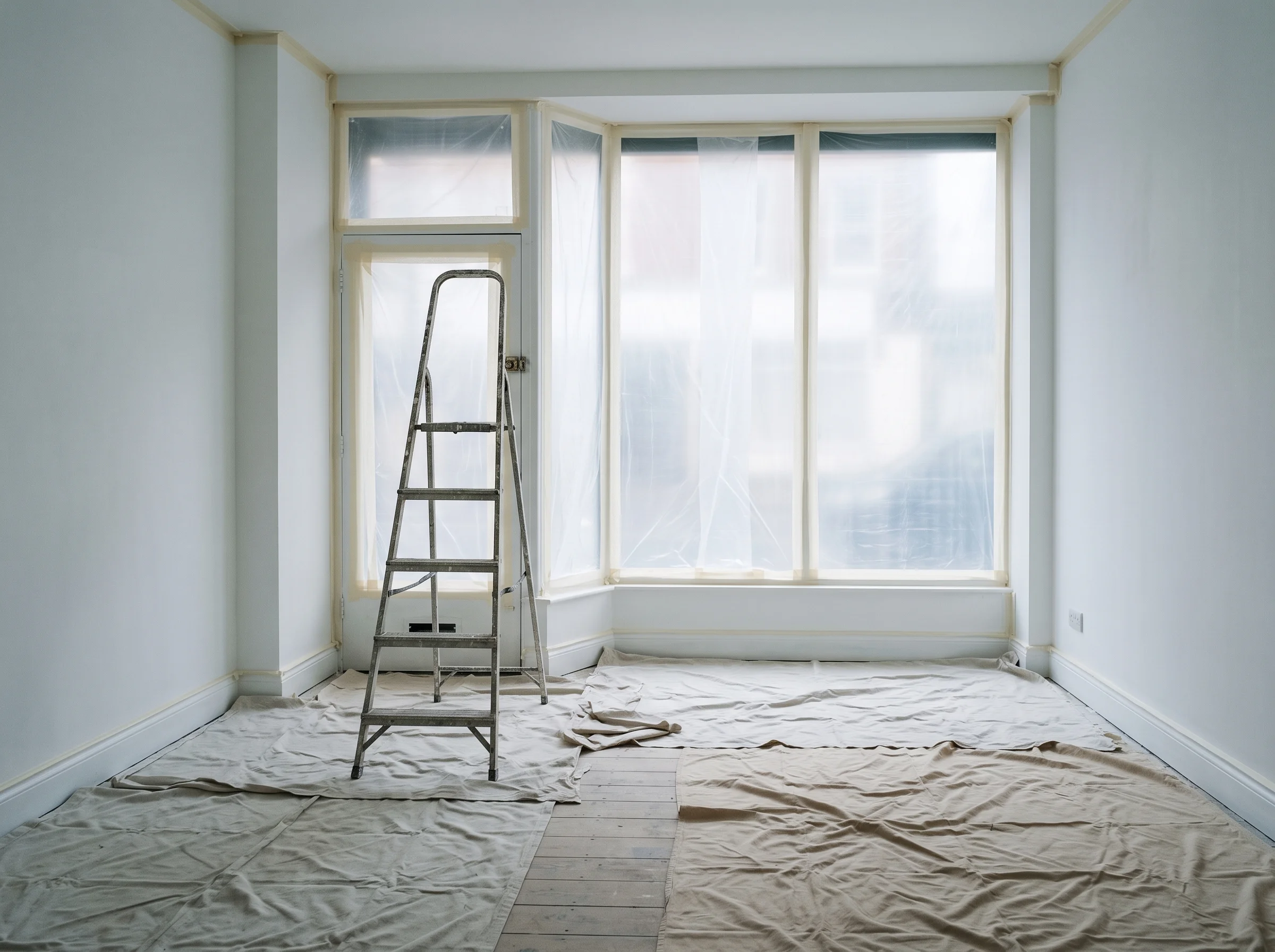 An empty commercial interior with masked shopfront glazing, fresh white walls and a stepladder on dust sheets